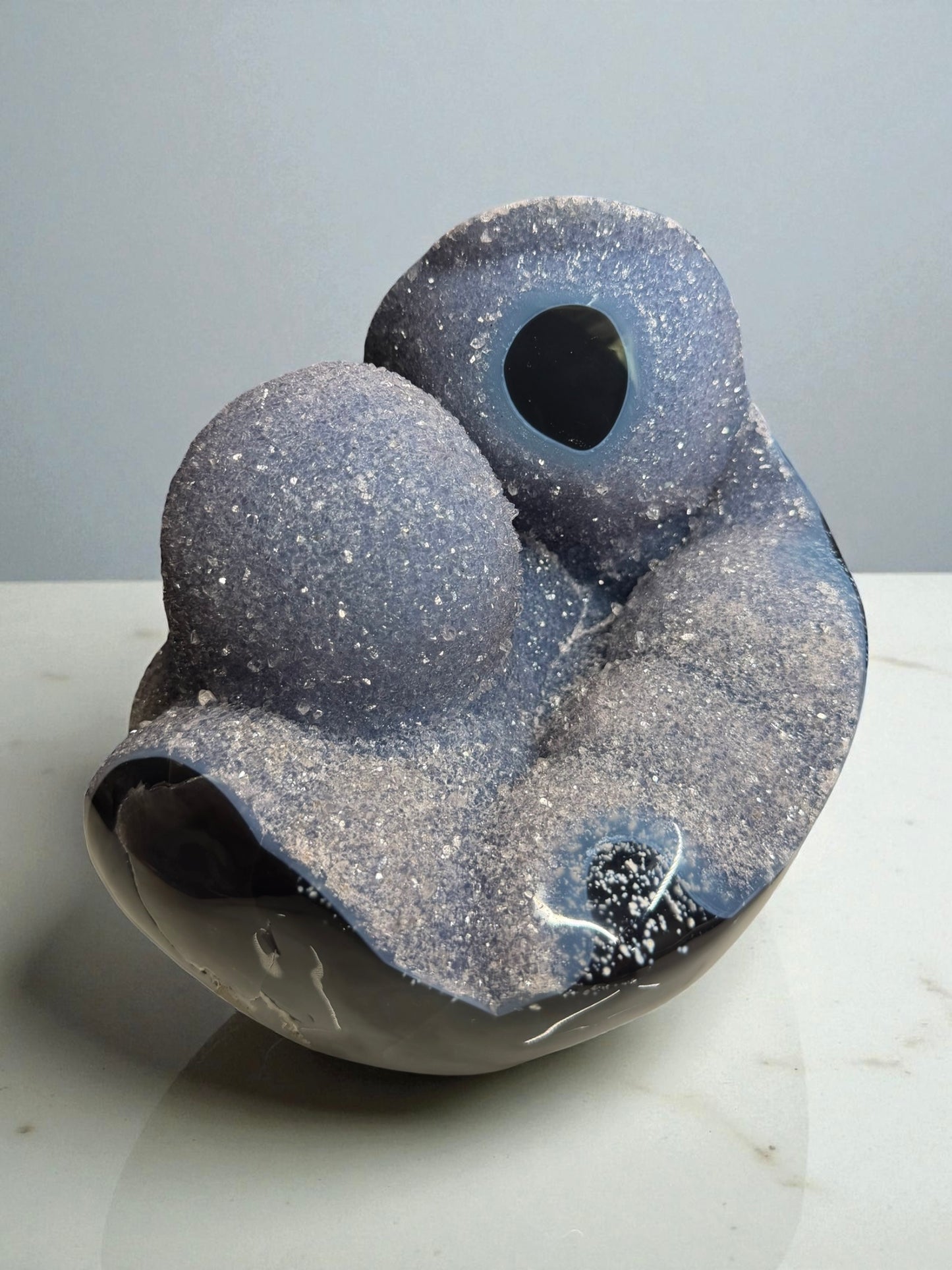 Large sculptural blue agate from Artigas, Uruguay featuring druzy bubbles and soft blue banding, photographed against a dark background.