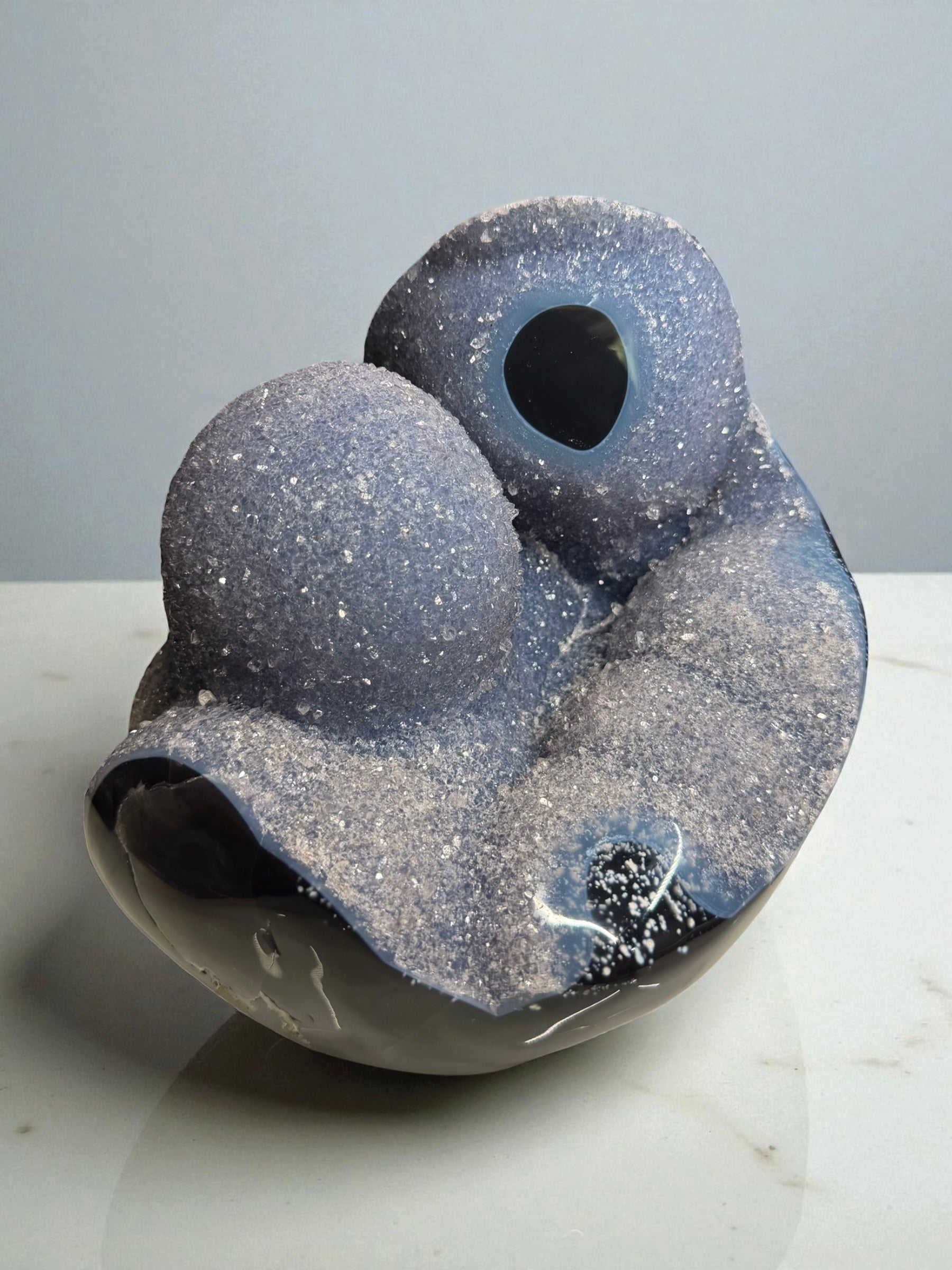 Large sculptural blue agate from Artigas, Uruguay featuring druzy bubbles and soft blue banding, photographed against a dark background.